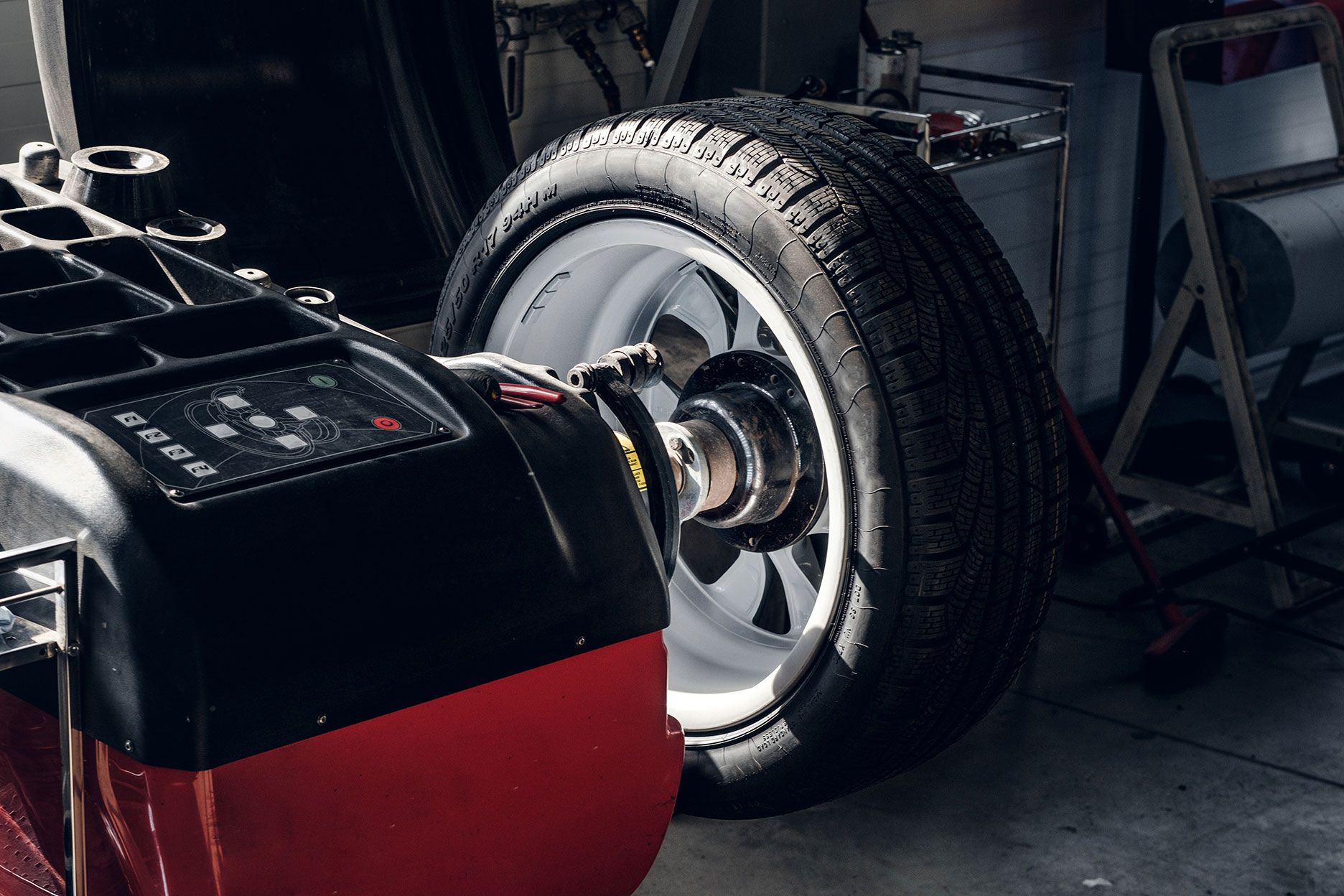 Tire being balanced on a machine in a garage; black tire on a white rim, red machine base.